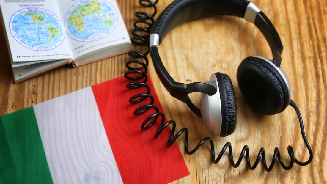 Headphone and book on a desk with an Italian flag.