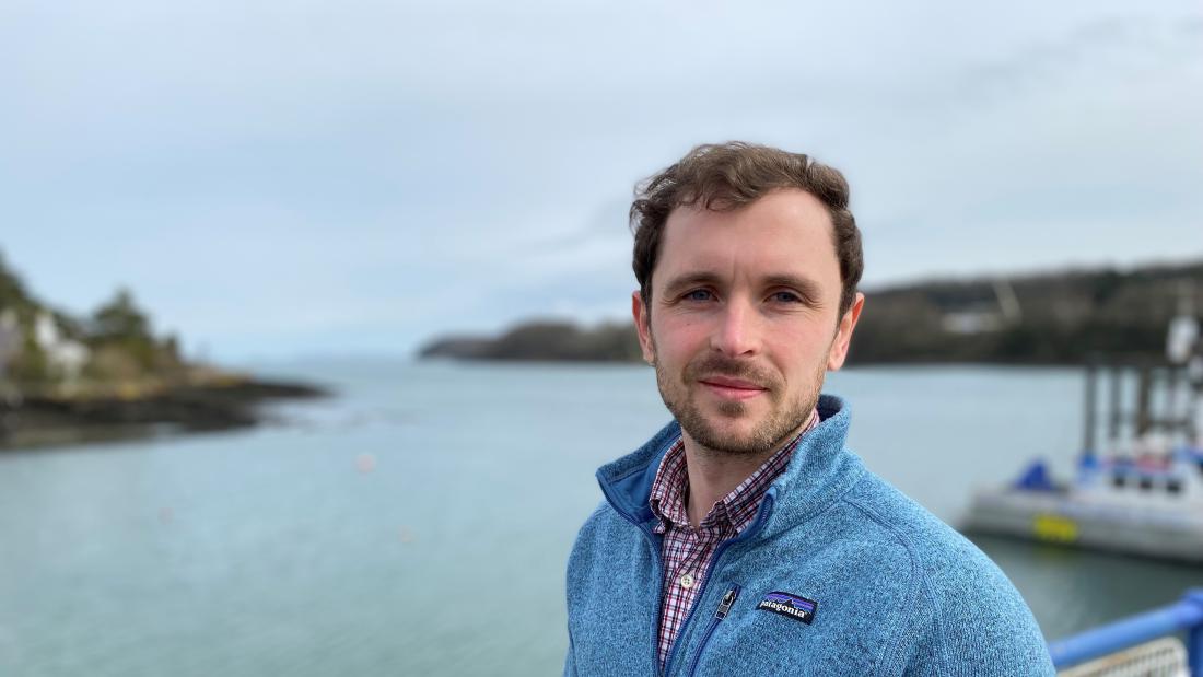 Young man stands on bridge with land and water out of focus behind him