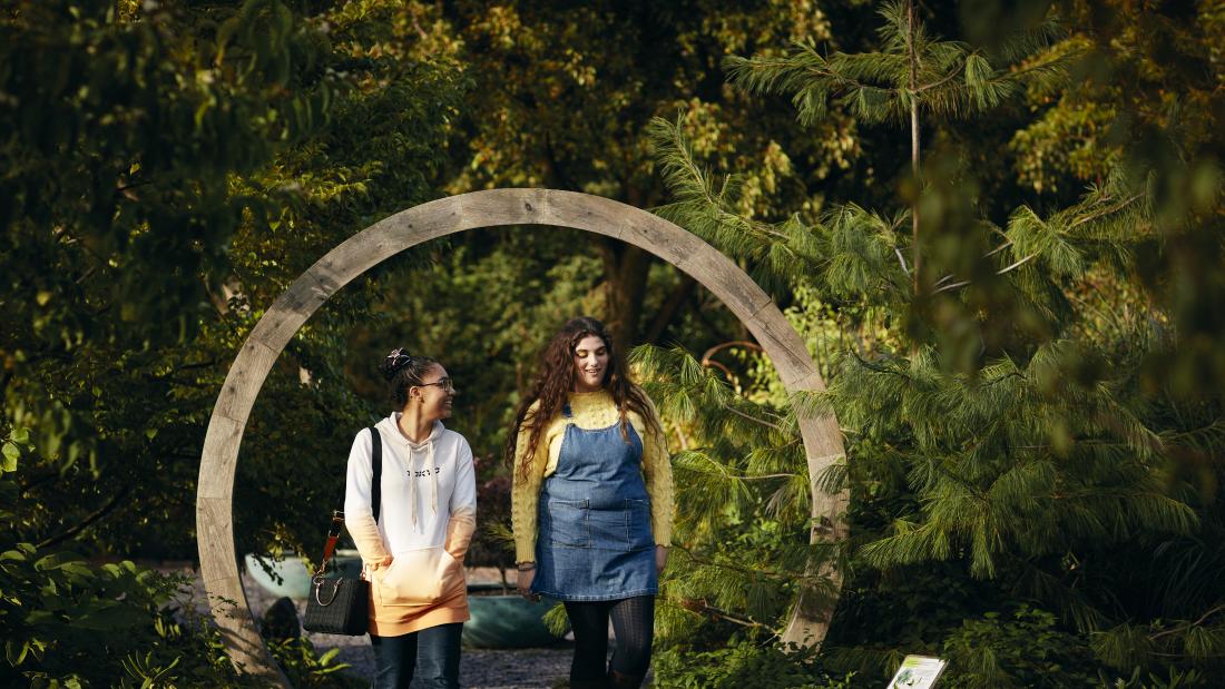 two students walk  among trees at Treborth Botanic Garden, Bangor University