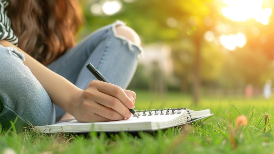 Girl writing in a notebook with sunset in background