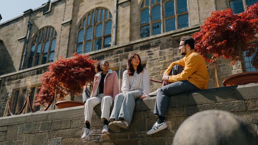Three students sitting on the wall in the inner quad, Main Arts Building