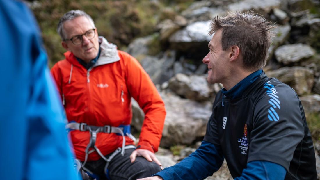 Two men, Michael Mosley with Professor Jamie Macdonald, sitting on the side of a mountain with climbing gear