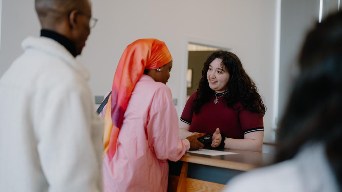 Two students speaking to a member of staff at a reception desk