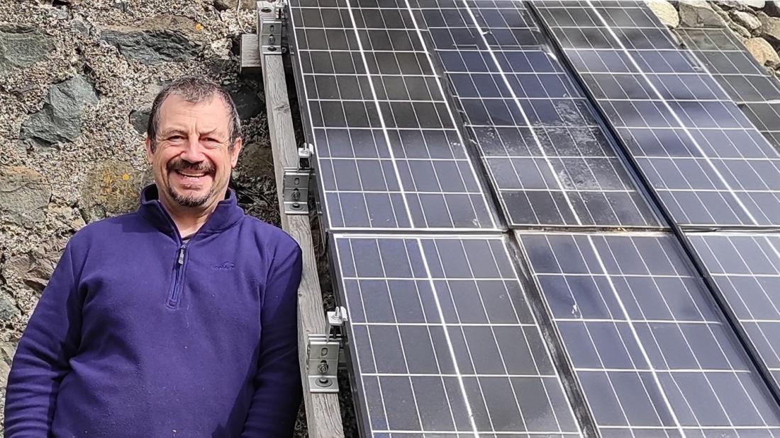 Dr Noel Bristow alongside a roof set of solar panels 