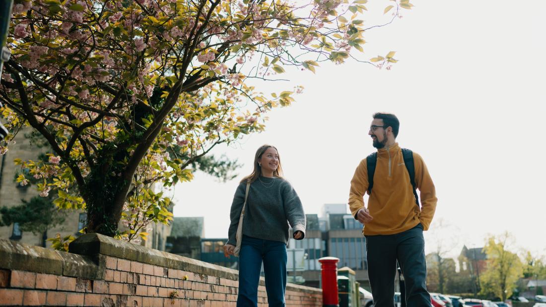 A photo of two students walking down the path outside Main Arts.