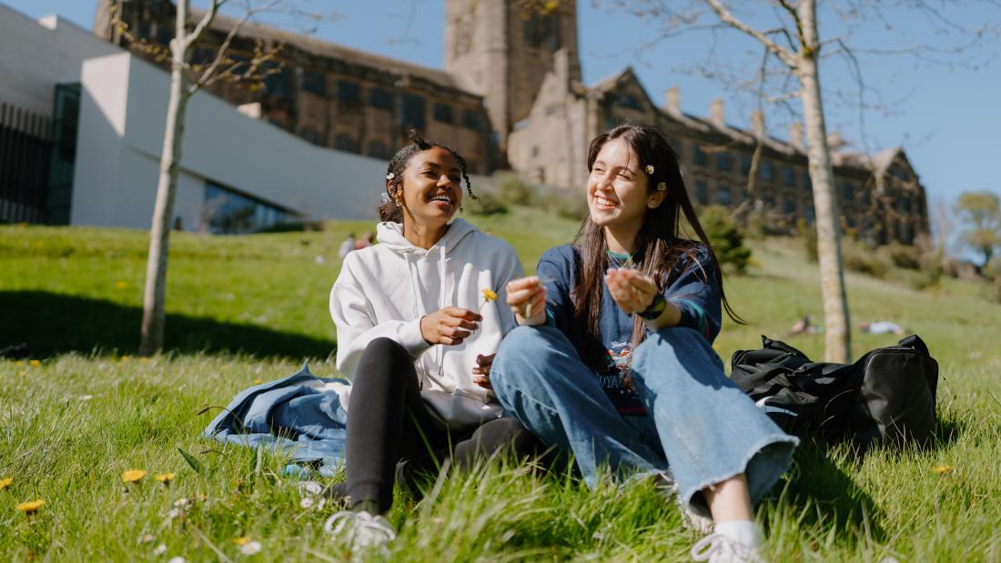 A photo of two students sitting on the grass talking to each other outside of Pontio.