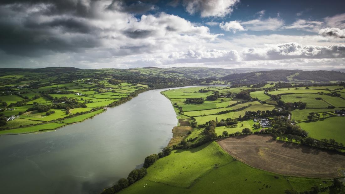 Aerial view of picturesque river valley between patchwork landscape with pastures, agricultural crops and rural homes.