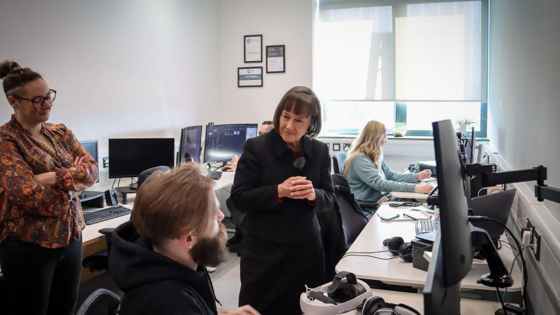 Secretary State for Wales speaking to person sat next to desk with big screen