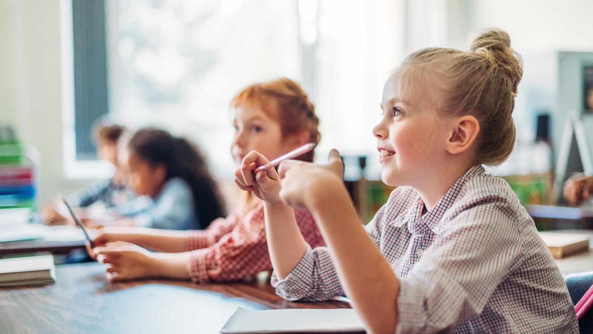 primary school children sat at a desk learning in classroom