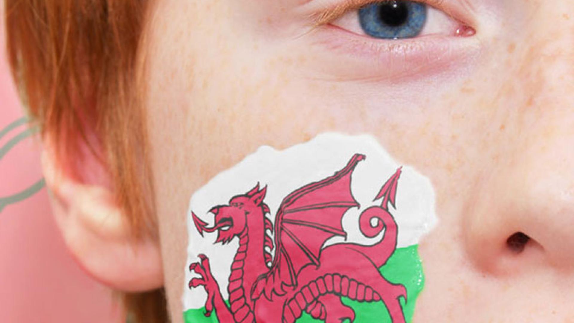 Plentyn gyda baner Cymru ar ei wyneb a baner Cymru yn y cefndir