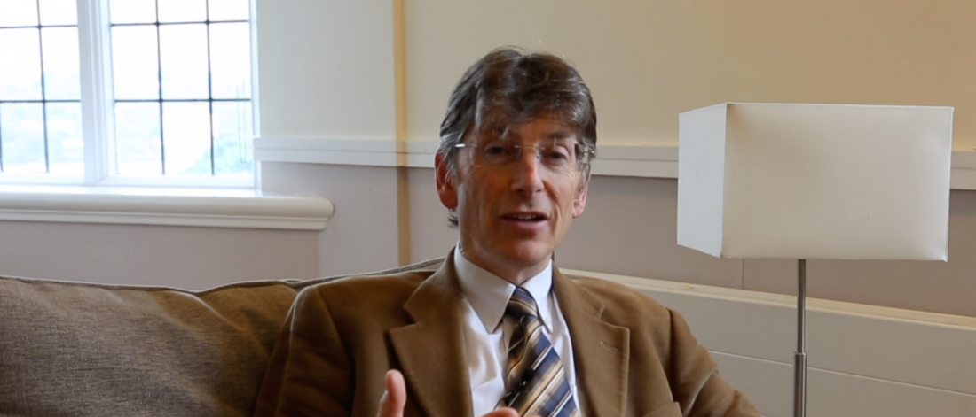 Image of a man wearing a brown suit sitting on a sofa 