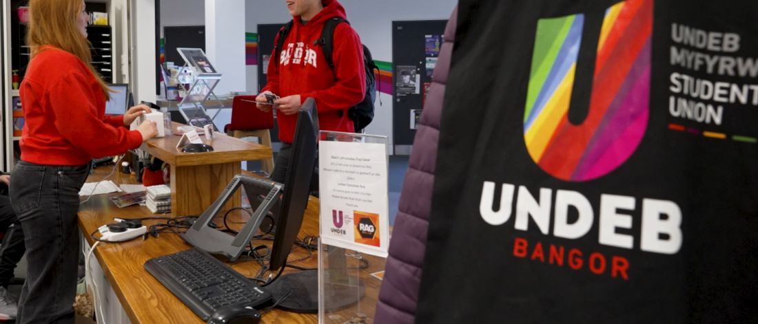 A student talking with a member of staff at the Undeb Bangor reception