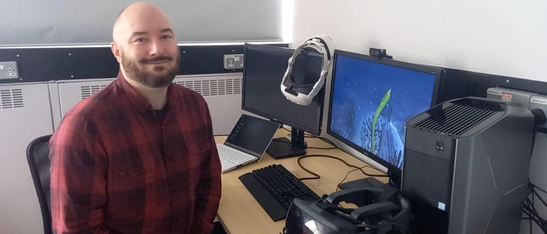 Llyr ap Cennydd sitting in front of a PC with VR underwater scene on the screen