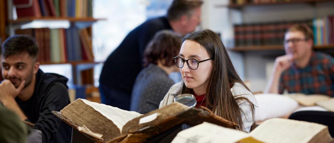 Student reading literature from large old book in a library