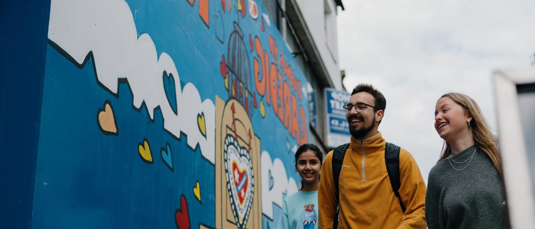 Three students walking in Bangor High Street next to wall mural