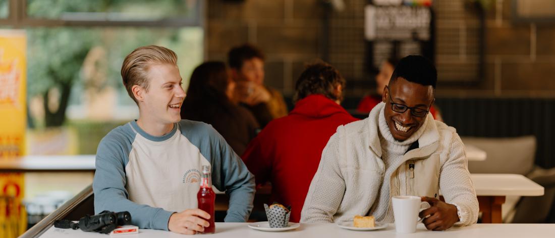 Two students sit laughing in Bar Uno, surrounded by groups of other students chatting and relaxing in the laid-back atmosphere.