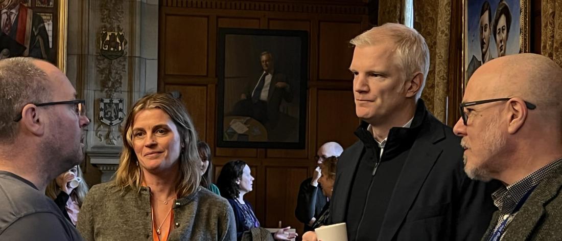 Image of three men and one woman chatting informally at an event