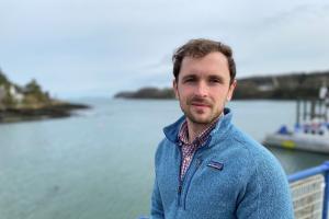 Young man stands on bridge with land and water out of focus behind him