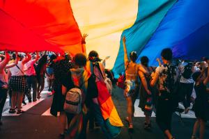 people parade under an enormous rainbow pride flag