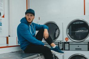 Man Sitting on Top of Washing Machine in Coin Laundry