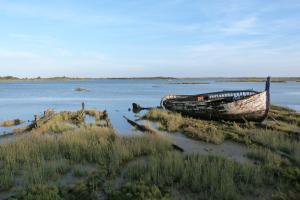  a wrecked boat lies at te edge of the water on a saltmarsh