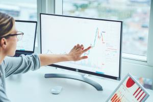 A woman points at a screen that is monitoring financial trends