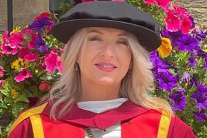 Doctoral researcher Meinir in a red and gold graduation gown