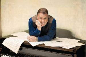 Bryn Terfel leaning over a piano holding sheet music