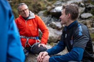 Two men, Michael Mosley with Professor Jamie Macdonald, sitting on the side of a mountain with climbing gear