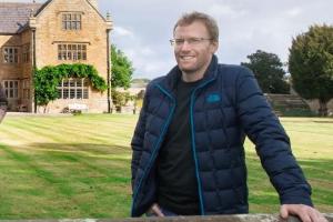 Dr Shaun Evans stands in front of a country house.