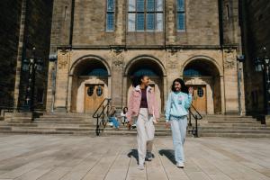 Two students walking towards the camera outside Main Arts