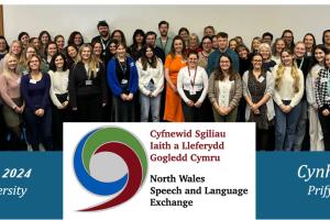 A large group of people stand smiling for the camera. Text on the image says 'North Wales Speech and Language Exchange Conference 2024, Wrexham University'