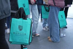 A queue of prospective students for the Open Day, the shot shows their legs and a pile of Open Day tote bags.