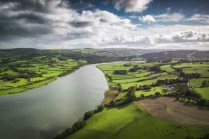 Aerial view of picturesque river valley between patchwork landscape with pastures, agricultural crops and rural homes.