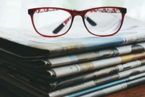 Reading glasses on pile of newspapers to denote NEWS