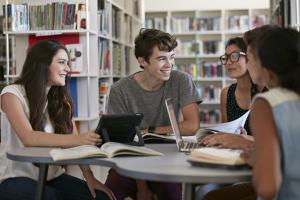 Students sitting at a table talking. On the table are laptops and books.