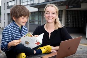 Young boy reading book with female smiling next to him