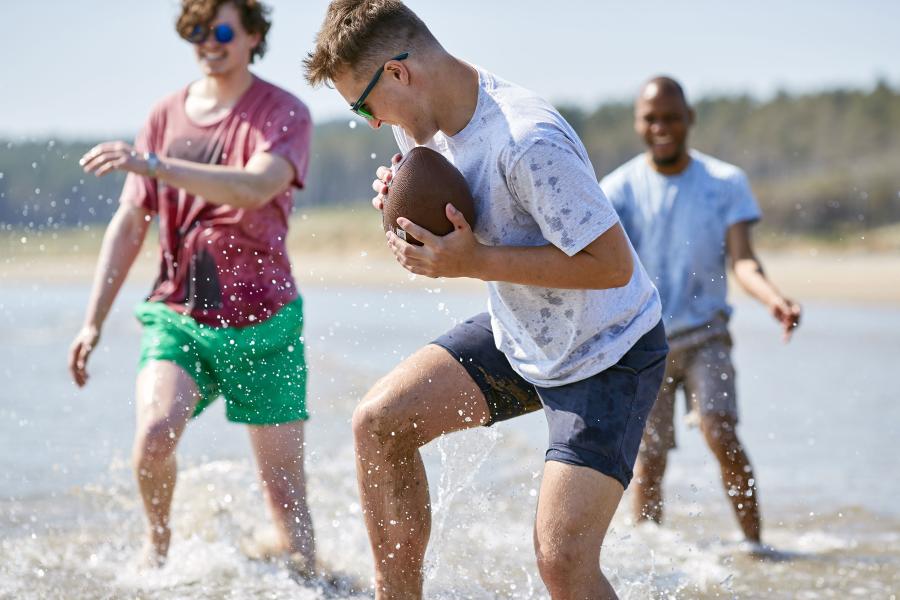 A group of students playing with a rugby ball in the sea on a nearby beach on Angelsey
