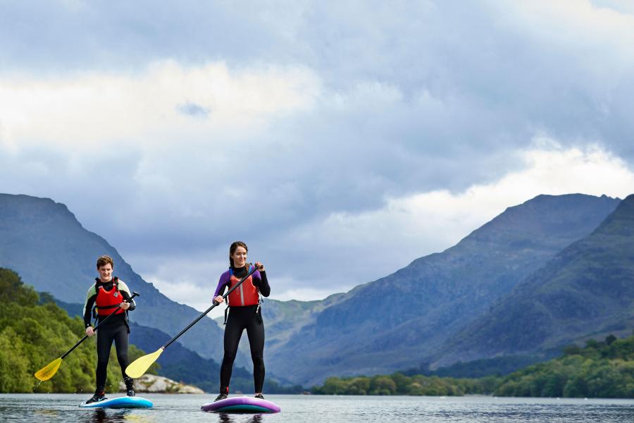 Myfyrwyr ar Fyrddau Padlo ar Lyn Padarn yn Llanberis gyda mynyddoedd Eryri yn y cefndir