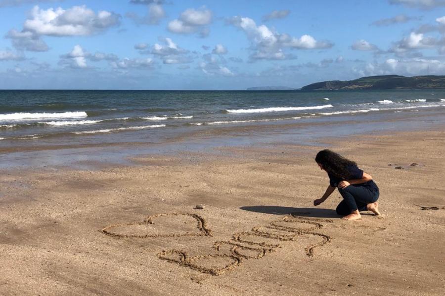 Student writing I Love Bangor in the sand on a beach during Welcome Week