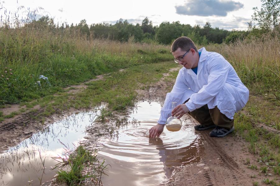 Laboratory assistant takes a water analysis in a puddle