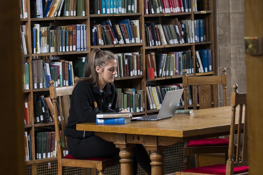 A student at work in the Library, books and laptop on the table