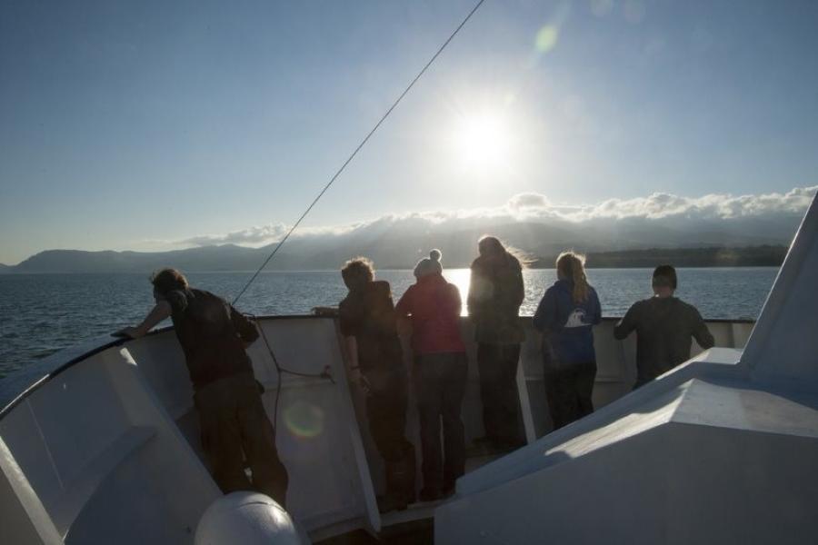 six people silhouetted against the bow of a ship with a low sun ahead.
