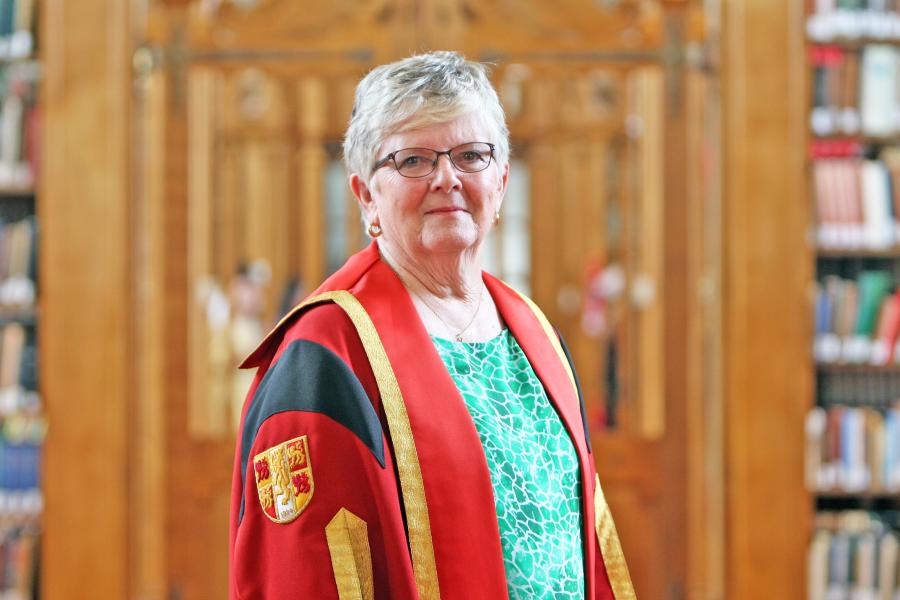 Woman with grey hair and glasses looks to camera in Bangor University library