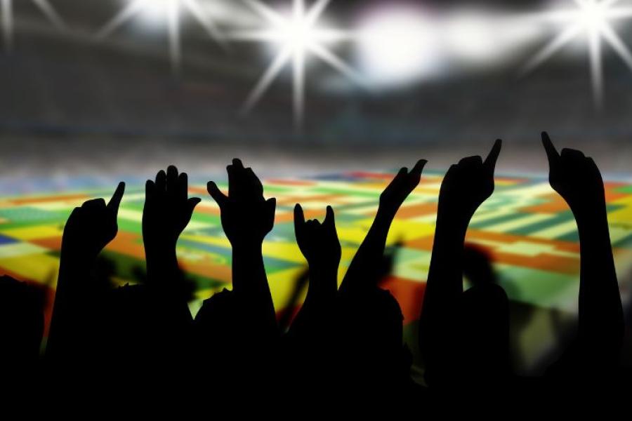 Hands in the air above footbball stadium showing flags of World Cup teams