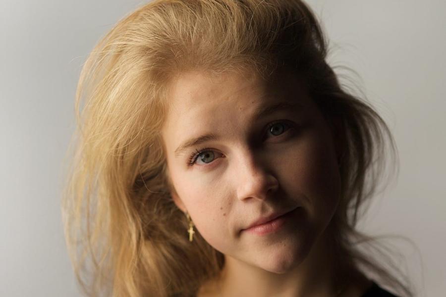  Girl with blond hair holds head to one side looking into camera