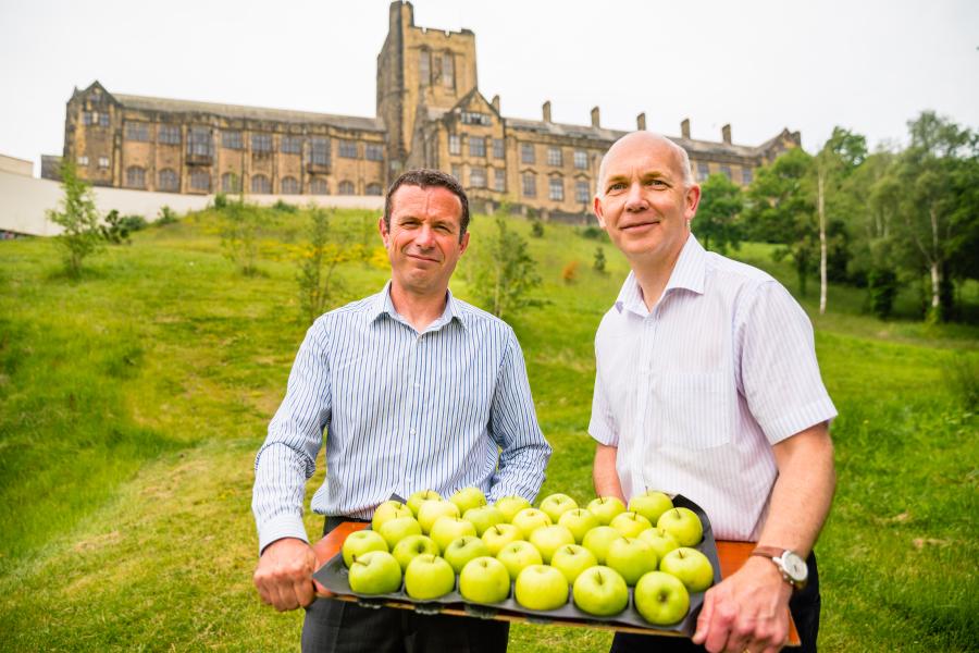 Twopeople holding a tray of apples outside with university in the backdrop