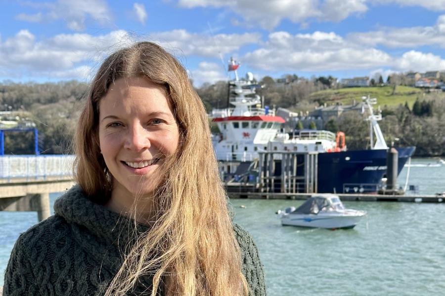 Image of Sophie Berenice Wilmes on the shore of the Menai Strait with the University's Research Vessel, the Prince Madog in the background