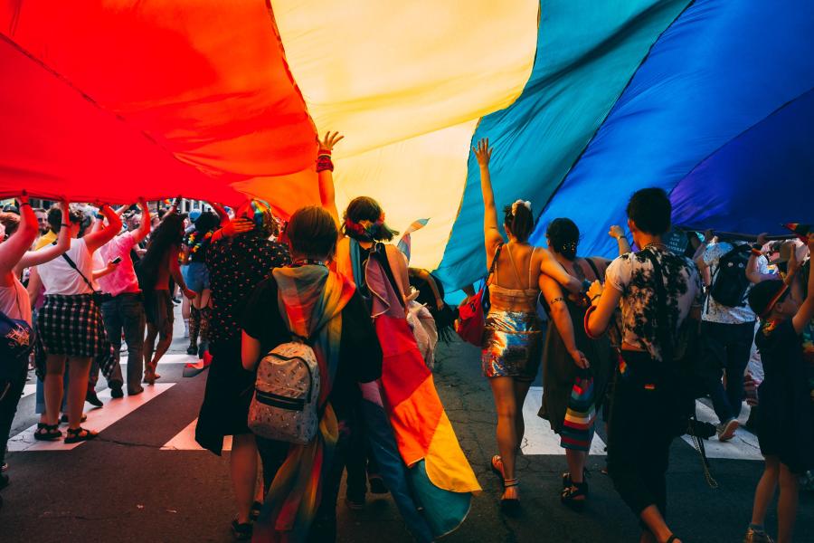 people parade under an enormous rainbow pride flag