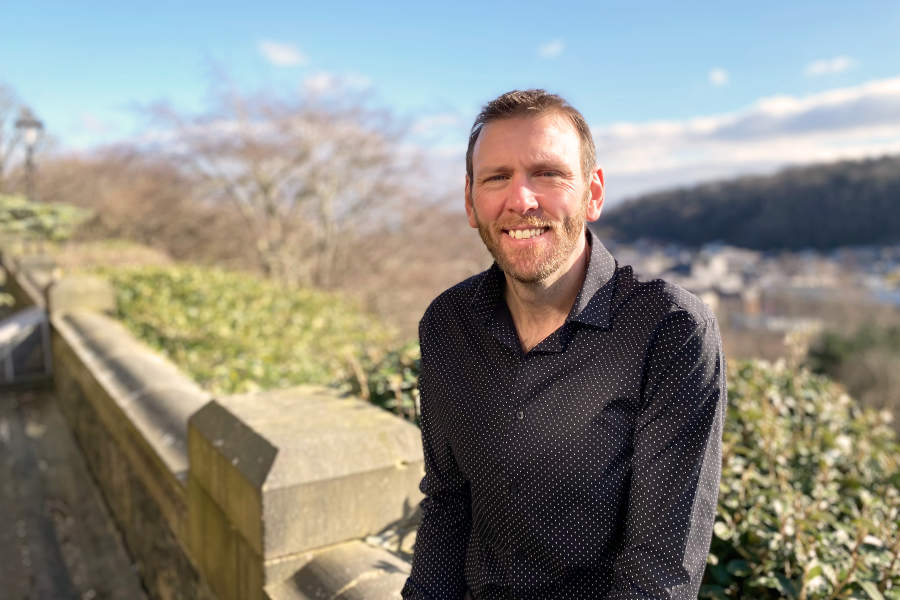 Person smiling whilst leaning against a stone wall with urban landscape in the background